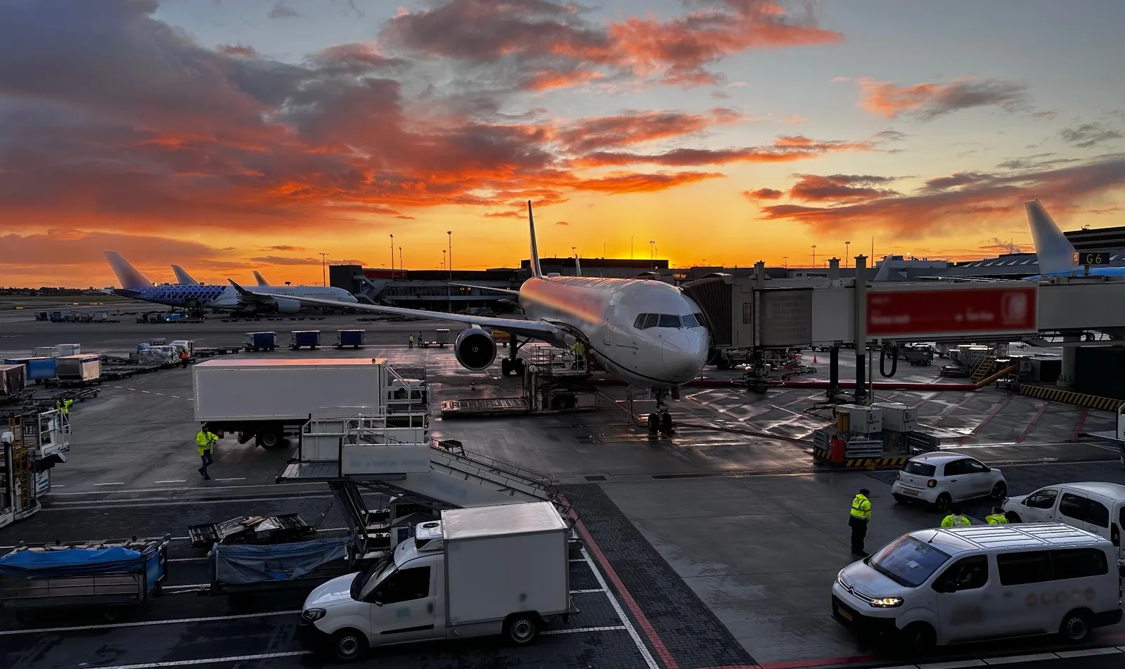 Commercial aircraft at airport gate during sunset with ground operations crew